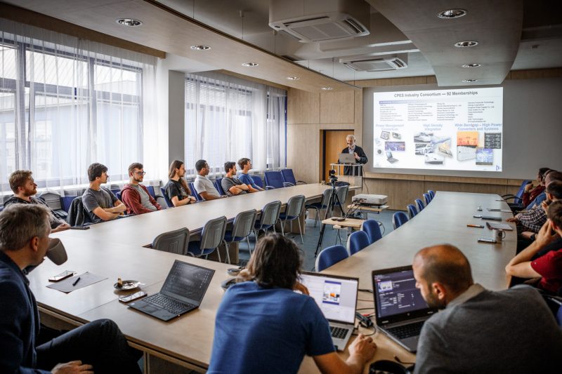 Professor presents a powerpoint presentation to a room full of students sitting at a large U-shaped table 