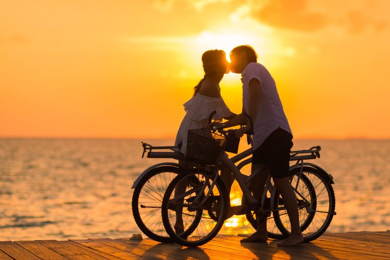 Couple kissing on beach while riding bikes at sunset.