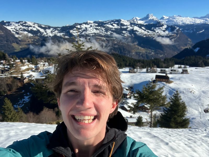 Eli Nichols smiling with a snowy mountain range behind him