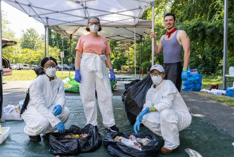 A group of people wearing protective clothing pose under a tent with two bags of trash in front of them. 
