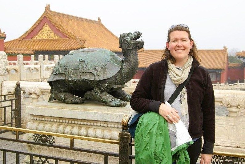 A person stands next to a sculpture of a turtle, with building behind her.