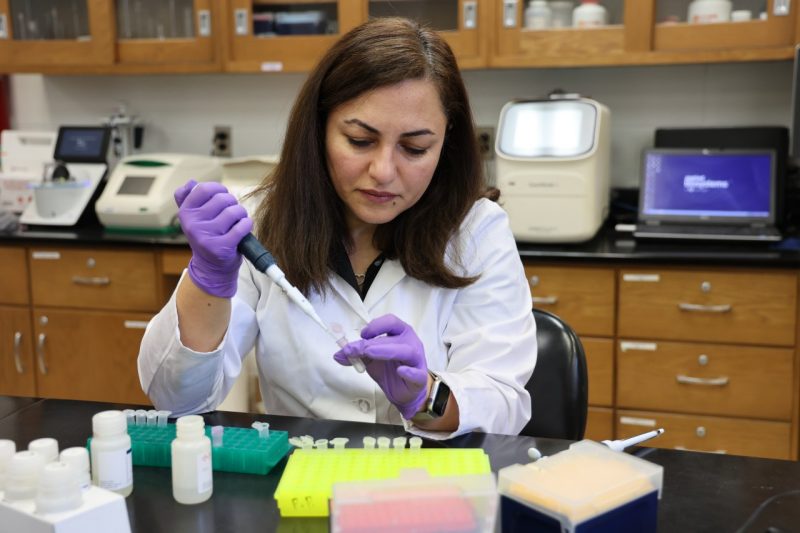 A woman in a lab coat uses a dropper inside a lab.