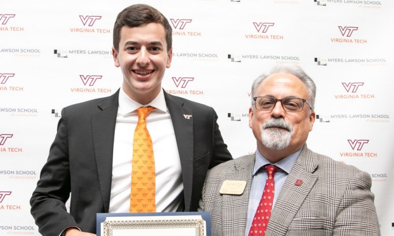 Student on the left smiles with a scholarship certificate in hand while his advisor on the right smiles and poses next to him.