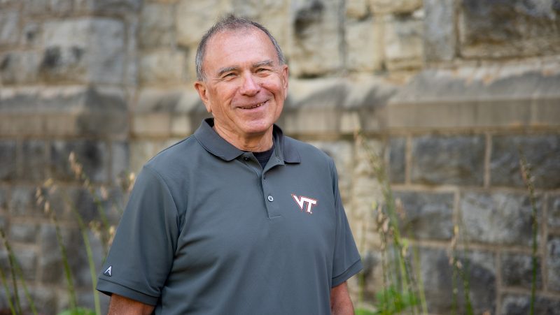 Robert Bodnar stands smiling in front of a wall made of Hokie stone.