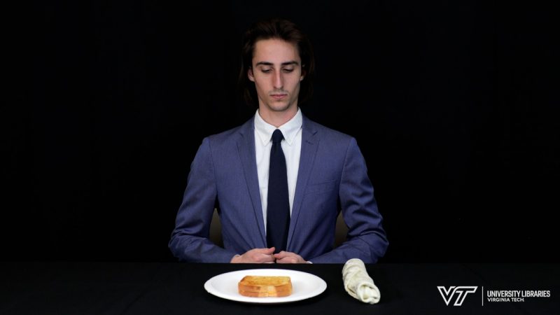 Dressed in a suit and tie, Jack is seated at a fancy table with a plate of grilled cheese, cloth napkin and silverware.