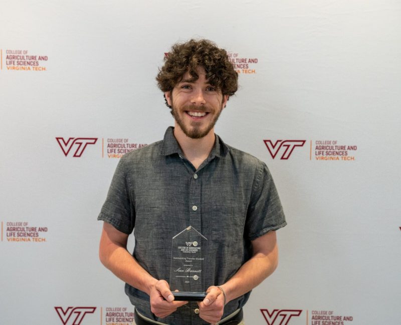 A smiling man holds a glass award plaque.