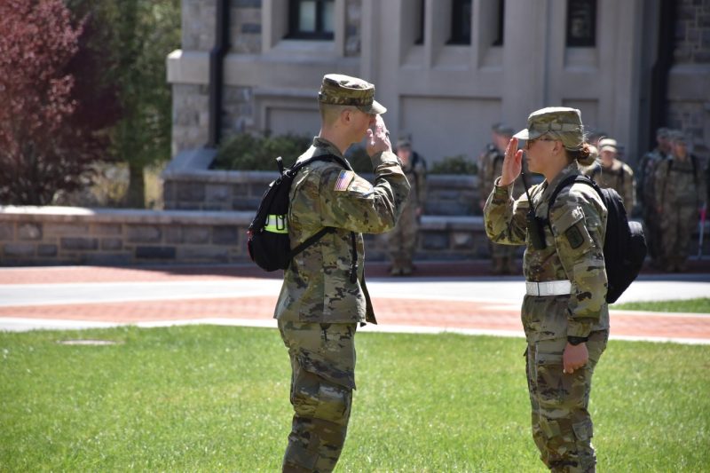 Butler is saluting Stevens and she is returning his salute while standing on the grass near Pearson Hall West.
