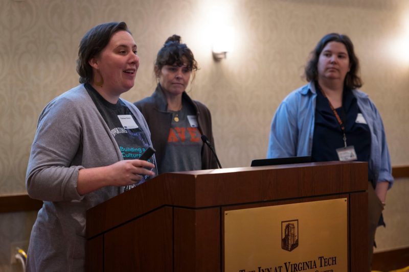 Chelsea Cleary speaks at a podium with Paige Bik and Rebecca Jarvis.