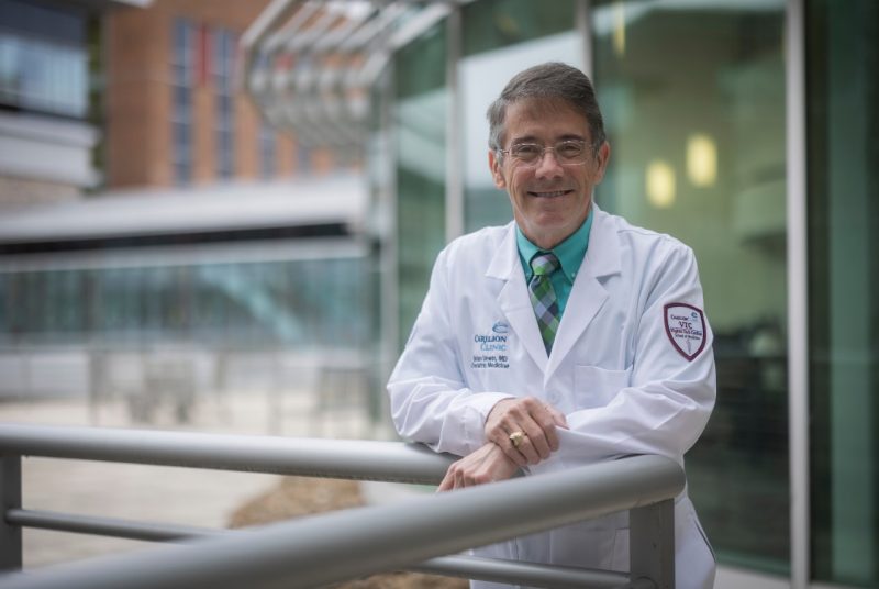 Man wearing doctor's coat leaning against outdoor railing.