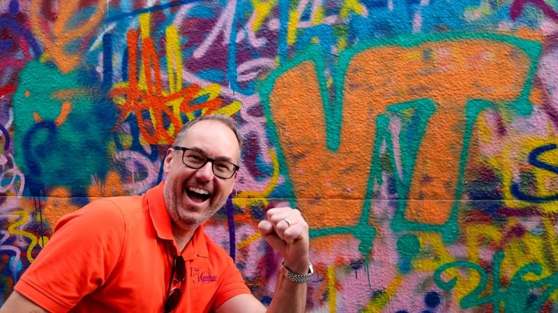 Man stands in front of art-covered wall.