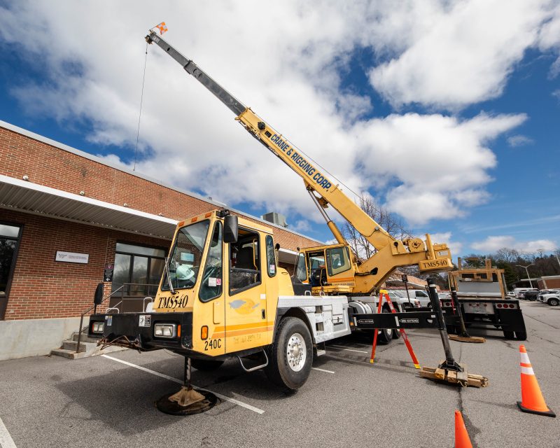 A large yellow crane is parked outside of Sterrett Center to deliver a new AC unitt.