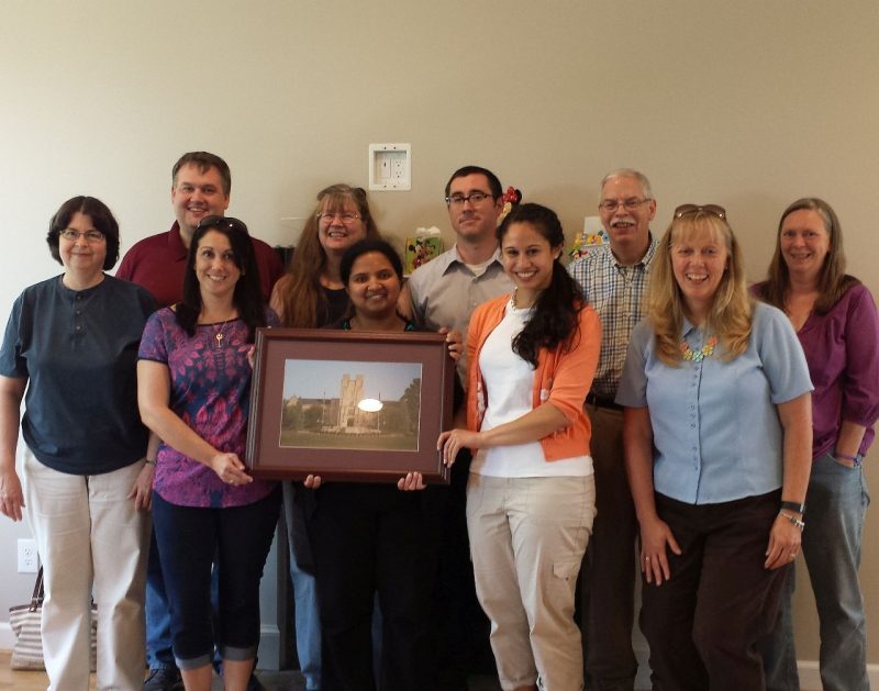 Colleagues take a group photo holding a picture of Burruss Hall.