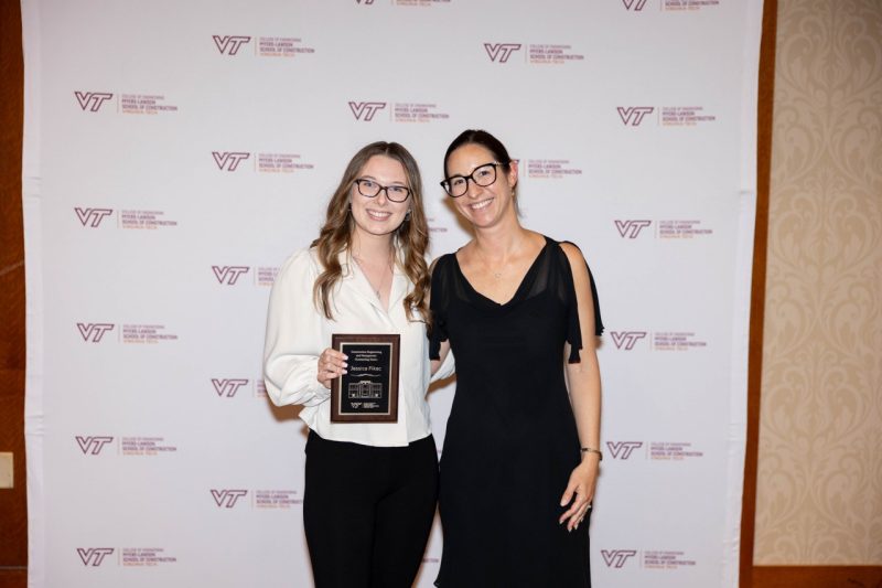 Woman at left holds an award while posing with woman at right.