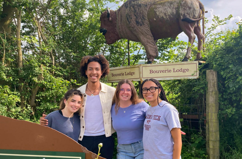 Four students pose beneath a wooden sculpture of a bison and a sign that reads "Bouverie Lodge"