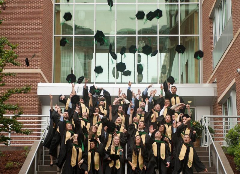 Students from the Class of 2014 toss their graduation caps while standing on the steps of the medical school building.
