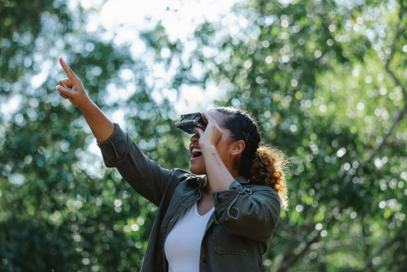 CNRE Kelsey Jennings (Lead) A person looks through a pair of binoculars in a forest.