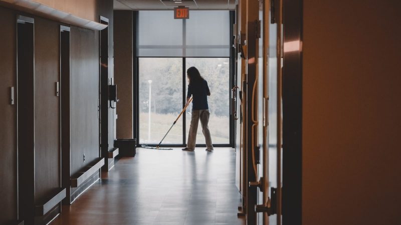 A Custodial Services employee mops at the end of a hallway