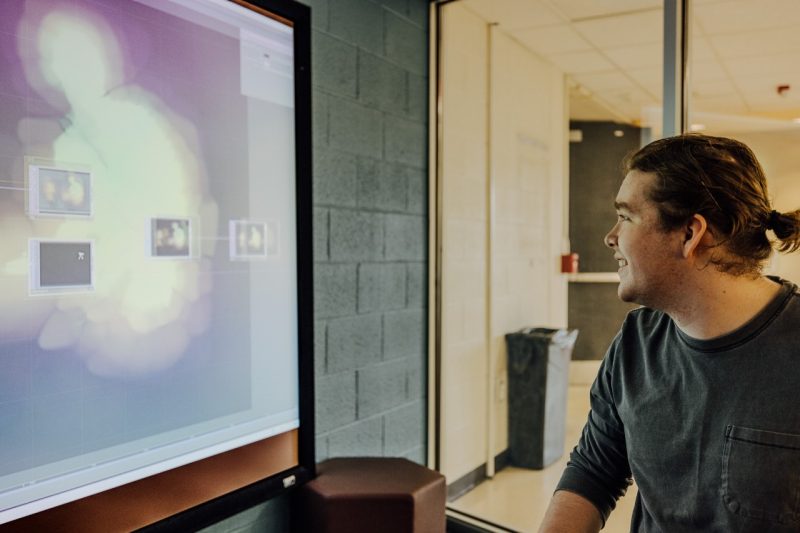 Intern Josh Taibbi looks at a large screen overlaid with a blob of color, where he's making changes to his video light installation.