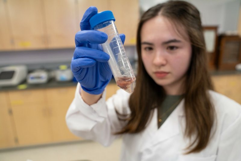 Kanna Yerks, wearing a white lab coat. holds up a test tube.