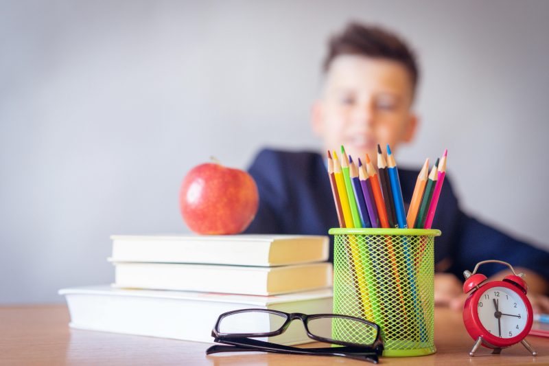 boy sitting behind a stack of books with apple and colored pencils