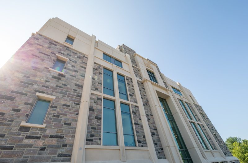 The sun shines on the left side of the grey Hokie Stone, precast concrete, and glass Undergraduate Science Laboratory Building.