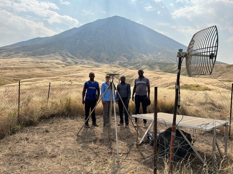 Four people in group shot with sensing equipment in the foreground and a giant mountain in the background.