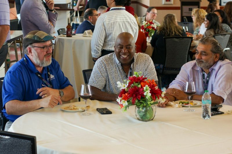 three men sit at a table laughing and eating appetizers
