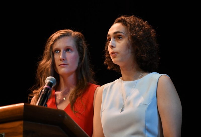 Two women stand side by side to speak at a podium. 