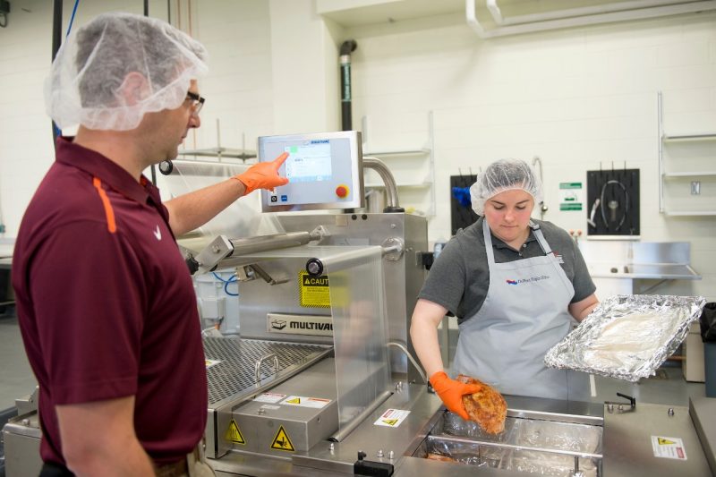 Man in maroon Virginia Tech polo and a hairnet shows how to properly package chicken for transport.