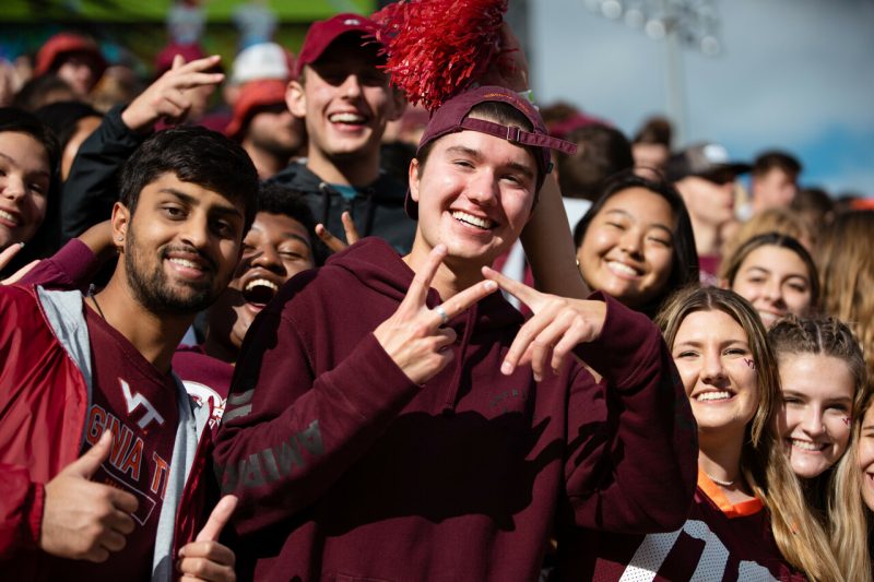 students in stands at football game holding up VT finger sign