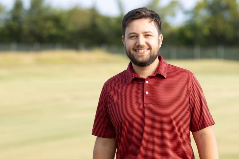 A smiling man posing in a field of grass