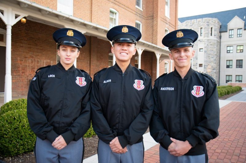Cadets in uniform stand smiling in front of the historic brick of Lane Hall.