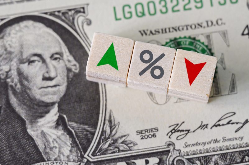 Percentage icon and arrow symbol on wooden cube in front of dollar bill