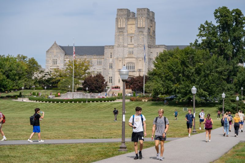 Burruss Hall is in the background with students walking along the drillfield.