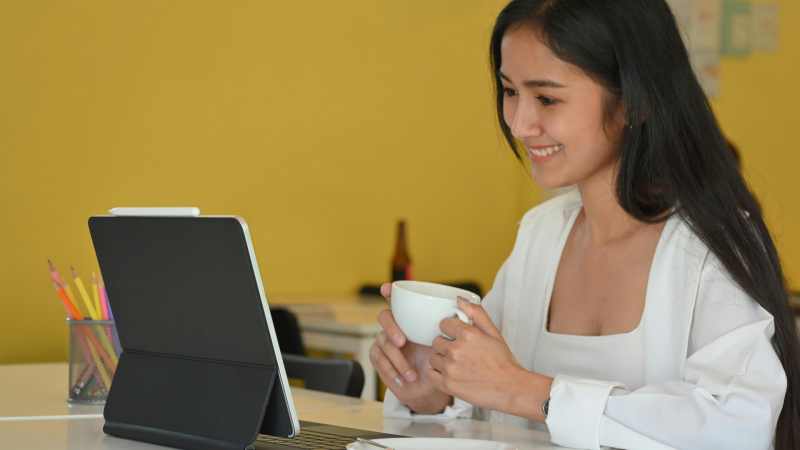 Brunette woman smiles while sitting at computer and holding a cup.