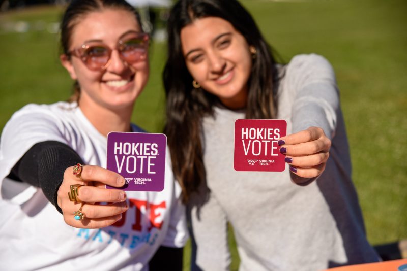 Two smiling students hold forward stickers reading "Hokies Vote."