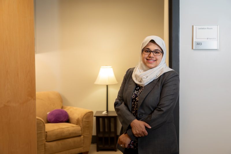 Graduate student and Diversity Scholar Ainul Huda stands smiling in the doorway of a warmly lit lactation room.