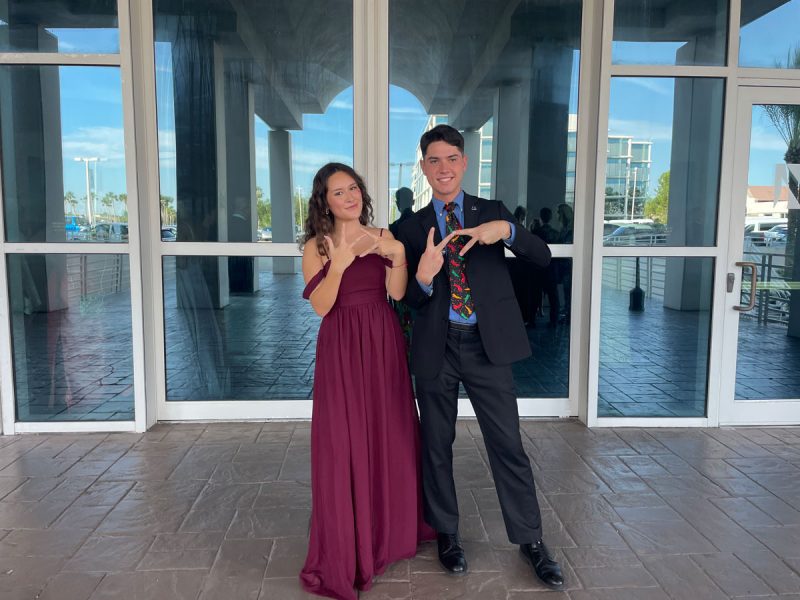 Two people dressed in fancy clothes flashing "VT" signs with their fingers.
