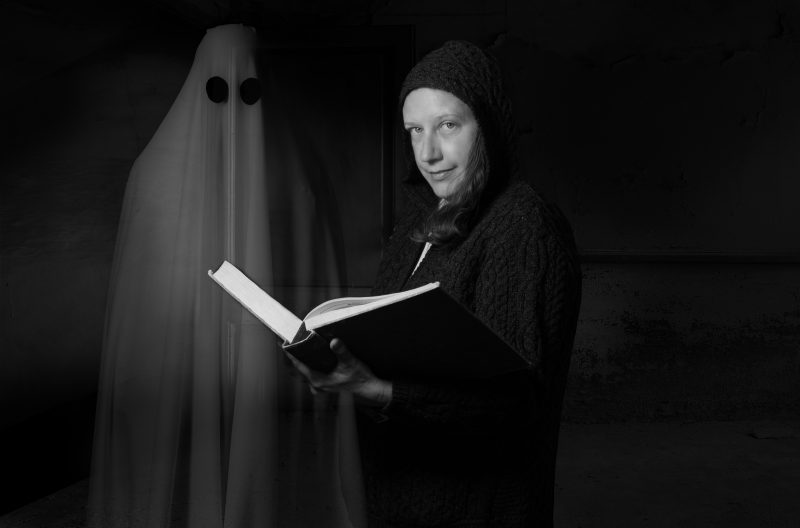 Ingrid Johnson holding a book with a ghost decoration hanging behind her. Photo by Leslie King for Virginia Tech.