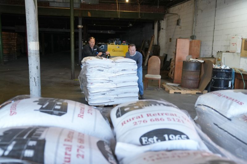 Two men load horse feed in a warehouse