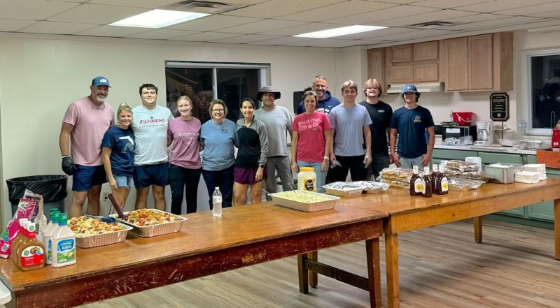 A group of smiling people standing behind a table of food