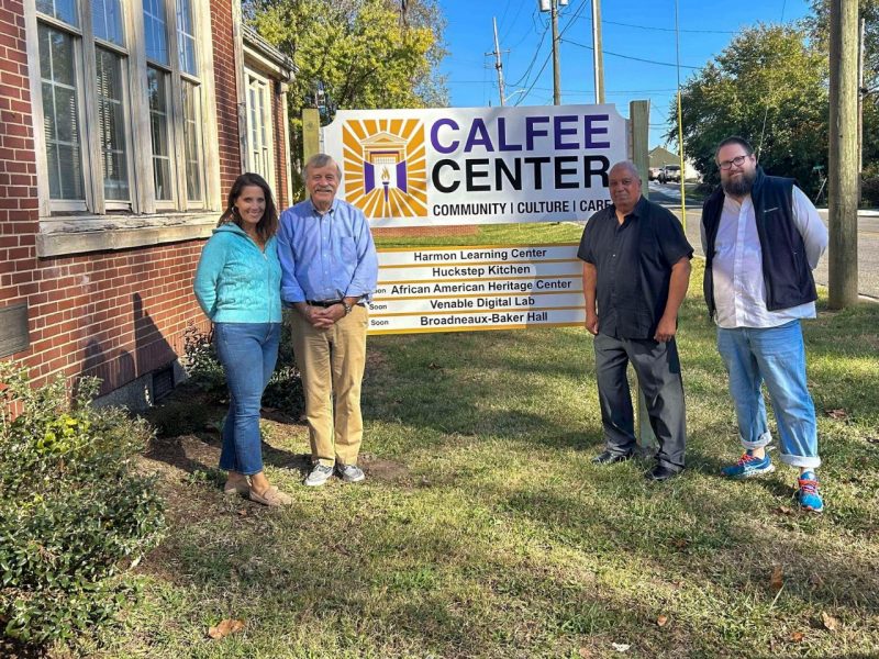Three men and a woman stand side by side, smiling, in front of the Calfee Cultural and Community Center sign.