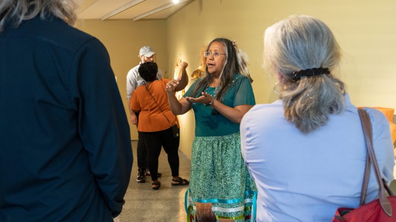 Vicky Ferguson leading art exhibit, Indigenous Peoples' Day 2023 Vicky Ferguson, in a green Monacan-style dress and donning a feather in her hair, guides visitors through an art exhibit for Indigenous Peoples' Day 2023.