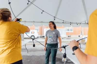 Elli stands under a large white tent with other volunteers as they work to hang string lights under the tent.