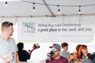 People sit at long tables in front of a banner that says "Making Downtown Christiansburg a great place to live, work, and play."