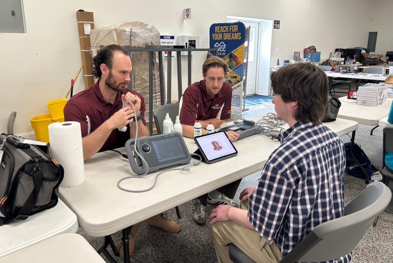Students at Monacan event Two men wearing VTCSOM shirts showing a younger man a portable ultrasound machine