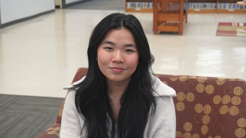 Hailey Richards Picture of a girl with long, dark hair and a white zip down jacket sitting on a couch.