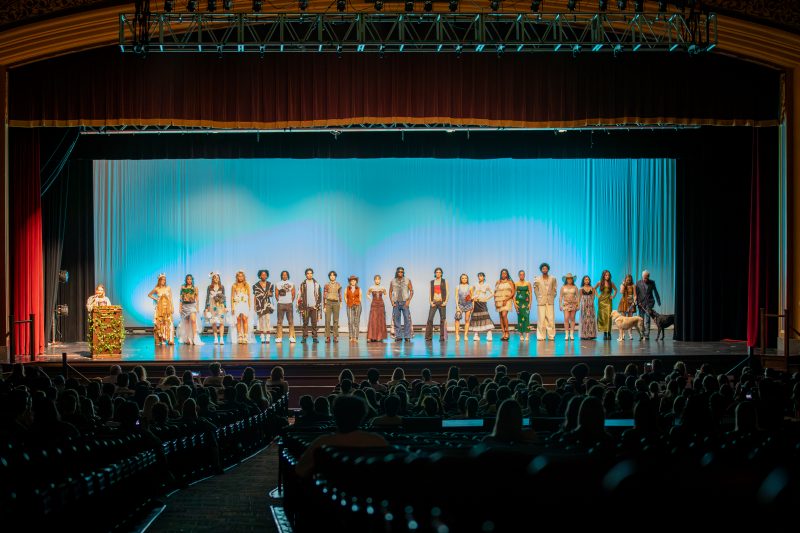 Over 20 individuals stand on a stage wearing sustainable fashion choices.