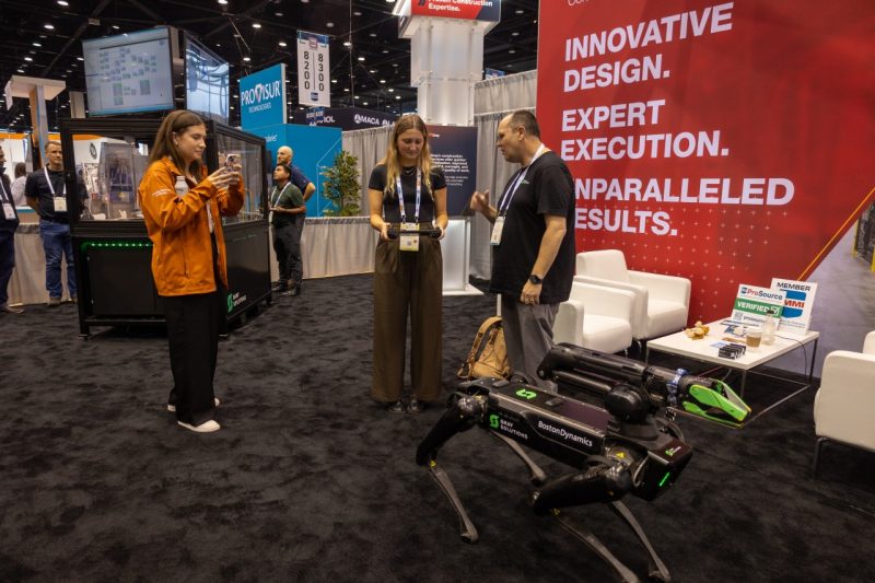 Two women stand near a robot dog.