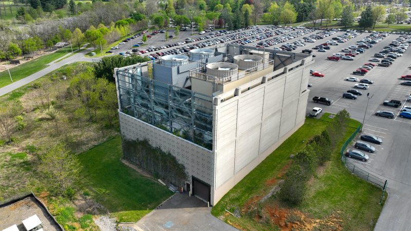 A drone photo of the Southwest Chiller Plant. The top of the building has large circular fans. The building is surrounded by a large parking lot and green grass.